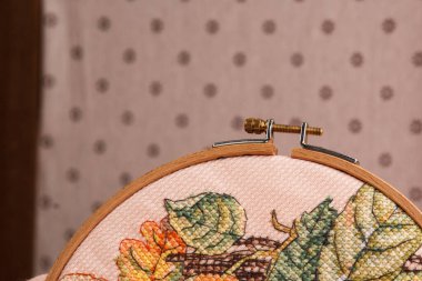 An embroidery hoop with a bright floral pattern is shot close-up against a pale pink background. Do-it-yourself aesthetic installation clipart