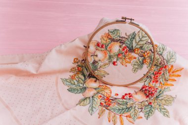 An embroidery hoop with a bright floral pattern is shot close-up against a pale pink background. Do-it-yourself aesthetic installation clipart