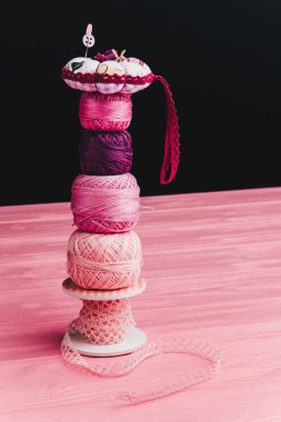 Siyah arka planda, örgü örmek için pembe ve mor çizgiler üst üste konur, en üstte de bir iğne yastığı bulunur.