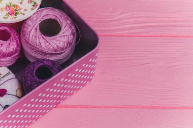 Pembe ahşap bir yüzeye renkli iplik topları ve dikiş malzemeleriyle dolu bir teneke kutu. El işi için mükemmel.