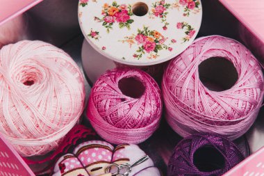 Pembe ahşap bir yüzeye renkli iplik topları ve dikiş malzemeleriyle dolu bir teneke kutu. El işi için mükemmel.