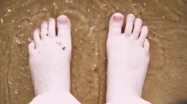 Bir insanın ayakları kumlu bir sahilde tatlı deniz suyuyla yıkanır. Barış ve sükunet kavramı olarak doğayla insan etkileşimi