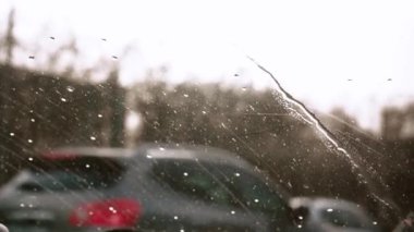Yağmur damlalarıyla arabanın ön camından görünen manzara. Yağmur damlaları ve camların arasından yağmurlu şehirde arabaların hareketlerini görebilirsiniz.