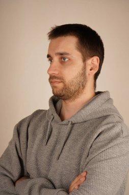 Genç bir erkek kameranın önünde duruyor. Adam kameraya bakıyor. Çapraz eller. Yan görüş. Yakışıklı adammış. Tarafsız bir arkaplan. Sıradan giyinmiş bir adam.