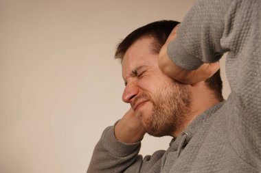 Genç adamın portresi elleriyle kulaklarını kapatıyor ve gözlerini gri renkte kapalı tutuyor. Umutsuz, sinirli sakallı adamın fotoğrafı ellerini kafasından ayırmıyor ve gözlerini kapatıyor. Depresyondaki adam