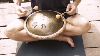 Tahta sopalarla davul çalan, yoga minderinde yan yana oturan, açık hava ortamında oturan birinin yakın çekimi.