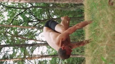 Bir adam ormanda yoga yapıyor. Yeşil bir hasırın üzerinde. Elleri dirseklerinin arkasında duruyor.