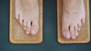 Ayaklarını ahşap bir akupres sadhu tahtasına yakın çekim yaparak doğal ayak terapisi ve rahatlama sağlıyor.