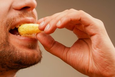 Young bearded man eating a ring-shaped snack holding it in his hand, closeup shot. Unhealthy but tempting fast food clipart