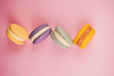 Çok renkli Fransız badem kurabiyeleri. Pembe arka planda düzgünce yerleştirilmiş. Mutfak sanatı ve tatlılığın mükemmel bir kombinasyonu hassas dokularını ve parlak gölgelerini vurguluyor.