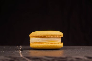 Pastel renkli badem kurabiyeleri, siyah arka planda. Sarı badem kurabiyeleri siyah bir masada yatar. Reklam tatlıları ve şekerlemeler için harika.