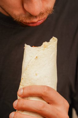 Elinde et ve taze salata ile doldurulmuş bir shawarma tutan aç bir adam büyük bir ısırık almaya hazırlanıyor. Ağız sulandıran sokak yemeği anları için mükemmel.