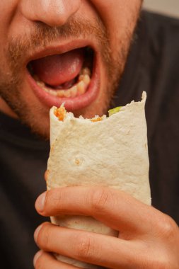 Bir adam et, salata ve taze sebzelerle dolu bir lahanadan bir ısırık almak için ağzını açar. Sakalı dinamik sahneye karakter katıyor.