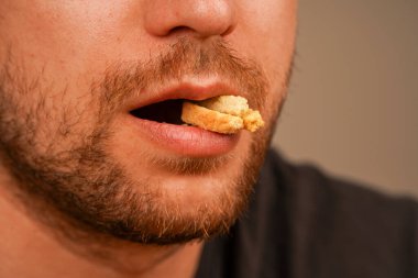 Erkeğin ağzındaki ruskların yakın çekimi aperatifin dokusunu ve zevk anını vurgular. Bir adam ağzına küçük gevrek bir aperatif alır, yemeye hazır.