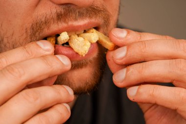 Bir adam ağzına küçük gevrek bir aperatif alır, yemeye hazır. Erkeğin ağzındaki ruskların yakın çekimi aperatifin dokusunu ve zevk anını vurgular.