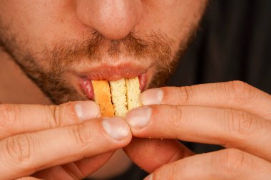 Kraker şeklinde çıtır çıtır atıştırmak üzere olan bir adamın yakın çekimi. Adam krakeri dişlerinin arasında tutuyor ve gevrek bir ziyafetin tadını çıkarıyor.