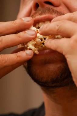 Patlamış mısırı elleriyle yiyen ve ağzına döken birinin yakın çekimi. Klasik abur cuburun dokusunu ve doğal hissini gösteriyor.