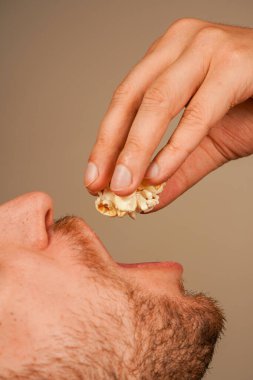 Patlamış mısırı elleriyle yiyen ve ağzına döken birinin yakın çekimi. Klasik abur cuburun dokusunu ve doğal hissini gösteriyor.