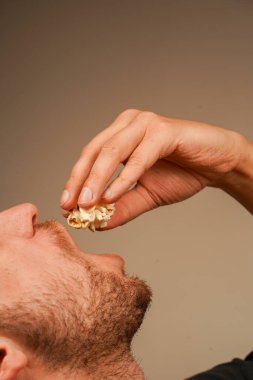 Bir adam taze patlamış mısırın tadını çıkarıyor, yakın plan bir çekimle yiyeceğin doğal dokusunu vurguluyor. Adam elinde patlamış mısır çekirdeği tutuyor.