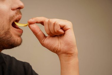 Sakallı bir adam elinde tutarken çıtır patates cipsini ısırıyor. Yemek reklamı ve abur cuburla ilgili görseller için harika.