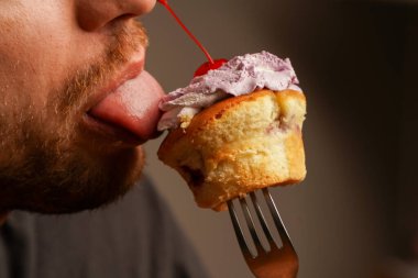 Siyah tişörtlü genç bir adam çatalla şişlenmiş bir keki yalıyor. Bir adam hevesle tatlı yer, yakın plan bir fotoğraf.