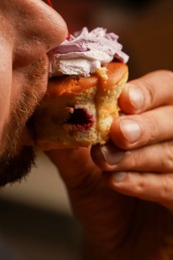 A man bites into a delicious pie with cherry filling and whipped cream. Ideal for food and confectionery concepts. A close-up of the process of eating sweets clipart