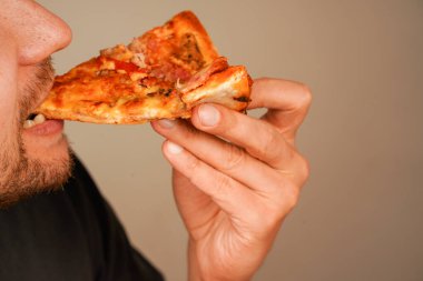 Bir adamın elinde peynirli ve pepperonili iştah açıcı pizza. Fast food, günlük yemek ve açlık kavramları için bir konsept.