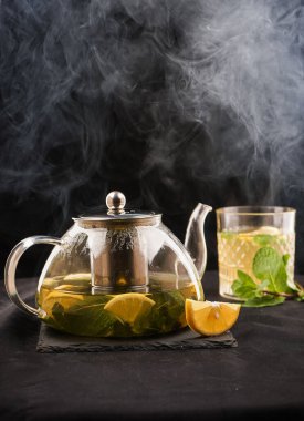 Çaydanlık demlenmiş çay, bir fincan çay ve yeşil yapraklı limon. Karanlık arka plan. Tarif