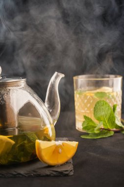 Koyu arkaplanda cam çaydanlıkta limonlu ve naneli zencefilli çay. Lemon da masanın üstünde. Kafe menüsü konsepti