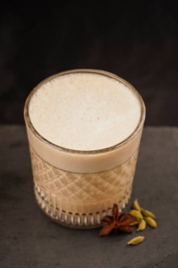 Ev yapımı çay sütlü latte anason ve tarçınlı çubuk ile tahta bir kırsal arka planda cam bardak ve siyah arka planda. Yakın plan fotoğraf.