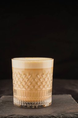 Güzel bir fincanda latte macchiato, izole edilmiş siyah arka planda, doğal gölgede. Şeffaf cam bardakta kapuçino köpüklü kahve ve süt içeceği. Sütlü Chai latte. Çay, sütlü kahve.