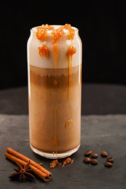 Sonbahar balkabağı aromalı latte, koyu bir masada kremalı. Sonbahar tatilleri için geleneksel bir kahve içeceği. Tarçın çubukları ve tahıllarla süslenmiş bir masa. Sonbahar zamanı.