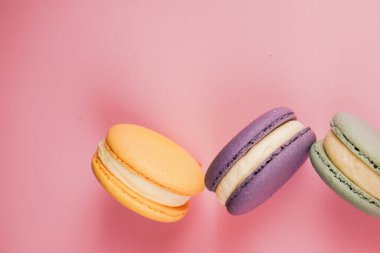 Pembe bir tabanda parlak renkli bir demet makaron. Lezzetli Fransız hamur işleri tat ve görsel zarafeti birleştirir.