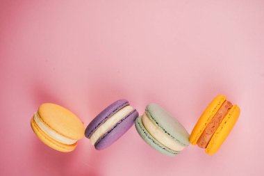 Pembe bir tabanda parlak renkli bir demet makaron. Lezzetli Fransız hamur işleri tat ve görsel zarafeti birleştirir.