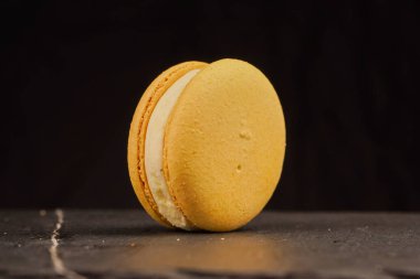 Pastel renkli badem kurabiyeleri, siyah arka planda. Sarı badem kurabiyeleri siyah bir masada yatar. Reklam tatlıları ve şekerlemeler için harika.