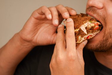 Elinde siyah ekmek, marul, domates ve meze ile katmanlı sandviç tutan bir adam. Rahatlatıcı yiyeceklere odaklanmış nefis bir an.