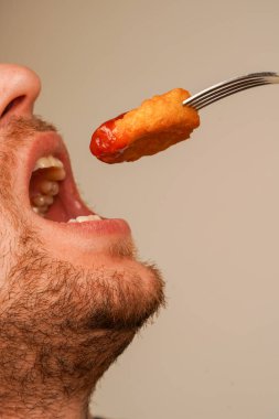 Taze hazırlanmış külçeler, çatalla şişlenmiş, tadını çıkarmaya hazır, fast food 'un zevkini sembolize ediyor. Külçeler ketçapla kaplanmış.