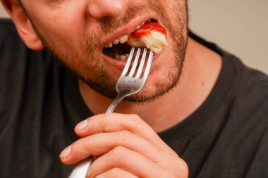 A close-up of a man eating a ketchup-dipped dumpling with a fork as he prepares to eat. The image captures the essence of home-cooked comfort food clipart