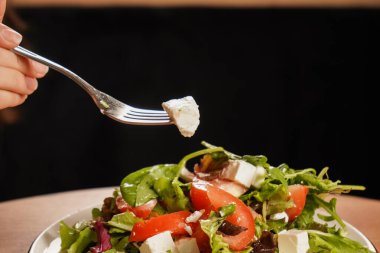 Canlı bir Yunan salatasına yakın plan, yeşil yapraklı, domatesli ve peynirli, tadını çıkarmaya hazır. Tahta masada bir tabak taze salata duruyor.
