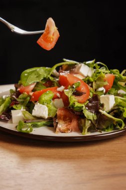 Canlı bir Yunan salatasına yakın plan, yeşil yapraklı, domatesli ve peynirli, tadını çıkarmaya hazır. Tahta masada bir tabak taze salata duruyor.