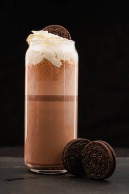 Chocolate milkshake with whipped cream served in a glass with a cookie in the middle on a dark table and black background clipart