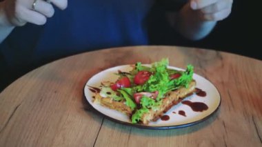 Fırında Belçika waffle 'ı ile yakın plan bir tabak domates ve soslu marul yaprakları. Sıcak bir kafedeki ahşap bir masada lezzetli bir tabak kahvaltı var.