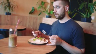 Bir adam mavi bir kanepede salata ve domatesli Belçika waffle 'ını seviyor. Yanında serinletici bir içecek oturuyor, sıcak ve rahat bir yemek sahnesi yaratıyor.