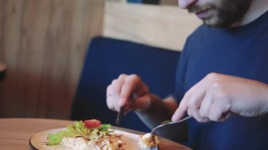 Bir adam mavi bir kanepede salata ve domatesli Belçika waffle 'ını seviyor. Yanında serinletici bir içecek oturuyor, sıcak ve rahat bir yemek sahnesi yaratıyor.