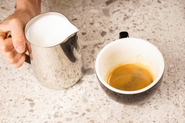 Kahve makinesinin yanındaki masada taze kahve ve süt ile siyah kupa.