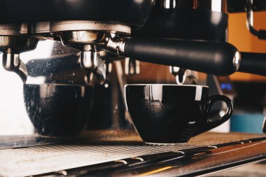 Profesyonel bir kahve makinesiyle bir kafede kahve yapmak. Yakınlarda boş bir fincan duruyor. Kahve makinesinde su damlaları görülebilir. Köpüklü kafe planı