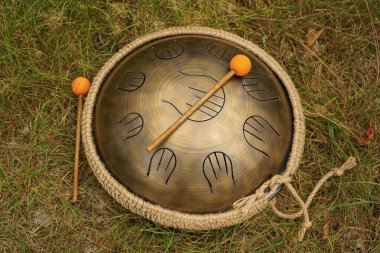 A handpan lies on the ground among the forest grass along with sticks with orange tips. The glucone is a percussion musical instrument that transmits many different tones clipart