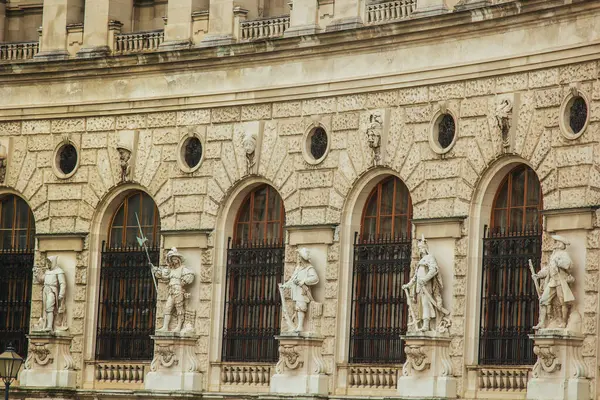 Viyana, Avusturya - 12 Mayıs 2019: Tarihi binanın çeşitli pozlarda klasik heykellerle süslenmiş görüntüsü. Ön cephe kemerli camlarla süslenir, her biri demir ızgaralarla kaplıdır.