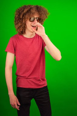 Kıvırcık saçlı ve modern gözlüklü çocuk, profesyonel ama genç ve yaratıcı bir görsel cazibe için canlı yeşil renk anahtarına karşı durarak, düşünceli bir şekilde mesafeye bakıyor.