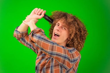 Düğmeli gömlekli kalın bukleli bir çocuk, saçını el yapımı budayıcı ile buduyor, parlak yeşil renk arka plan yaratıcı ve multimedya uygulamaları için sonsuz olanaklar sunuyor.